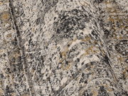 Nahaufnahme eines Designer-Teppichs mit abstraktem Muster in Grau-, Beige- und Goldtönen, aus seitlicher Perspektive aufgenommen.