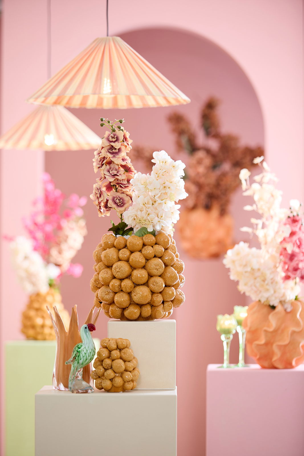 Dekoratives Ornament aus goldenen Kugeln mit Blumenarrangement, im Vordergrund mit pastellfarbenem Hintergrund und hängenden Lampen.