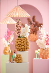 Dekoratives Ornament aus goldenen Kugeln mit Blumenarrangement, im Vordergrund mit pastellfarbenem Hintergrund und hängenden Lampen.