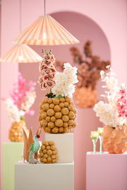 Dekoratives Ornament aus goldenen Kugeln mit Blumenarrangement, im Vordergrund mit pastellfarbenem Hintergrund und hängenden Lampen.