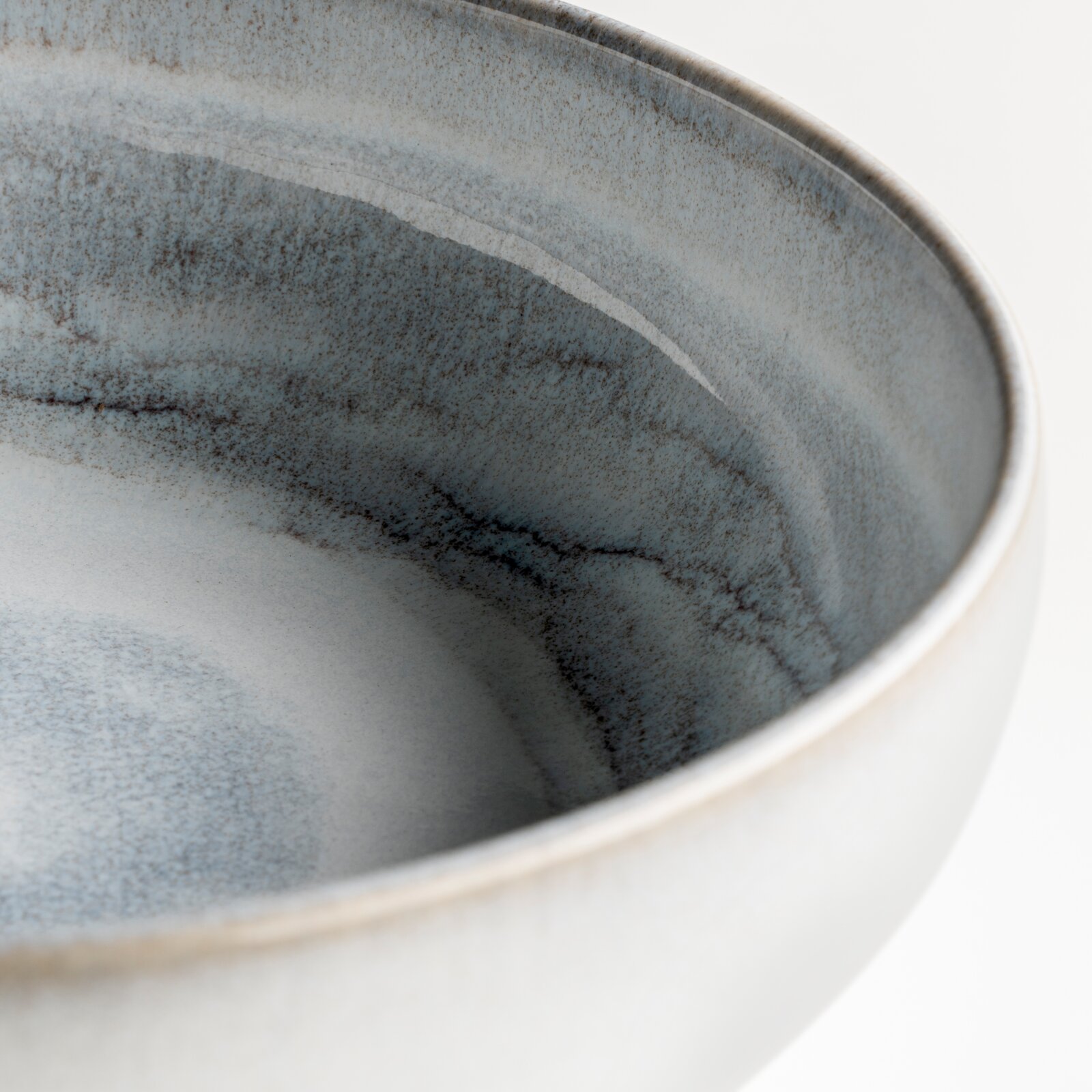 Nahaufnahme einer runden Keramikschale mit grau-blau gesprenkelter Glasur, schräg von oben in die Schale fotografiert