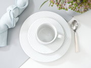 Kaffeeservice bestehend aus Tasse, Untertasse und Teller in eleganter weißer Optik, von oben fotografiert, mit Besteck und Serviette arrangiert.