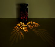 Solarleuchte mit floralem Muster, das warme Licht- und Schattenspiele auf den Boden projiziert. Perspektive von schräg oben.