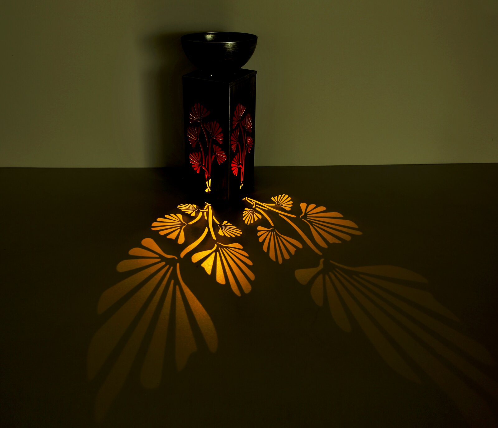 Solarleuchte mit floralem Muster, das warme Licht- und Schattenspiele auf den Boden projiziert. Perspektive von schräg oben.