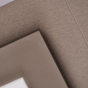 Detailaufnahme aus schräger Nahperspektive einer braunen, rechteckigen Platte vor einer holzartig strukturierten Oberfläche in warmem Graubraun