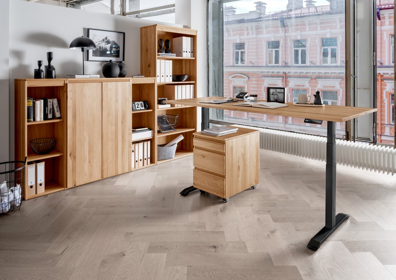 Moderne Büromöbelkombination aus Holz mit höhenverstellbarem Schreibtisch, Rollcontainer und Regalen, seitliche Perspektive.