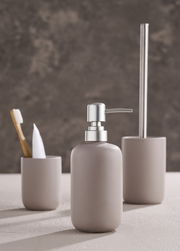 Modernes dreiteiliges Badset in neutralen Tönen, bestehend aus Seifenspender, Zahnbürstenhalter und Toilettenbürstenhalter, aus seitlicher Perspektive fotografiert.