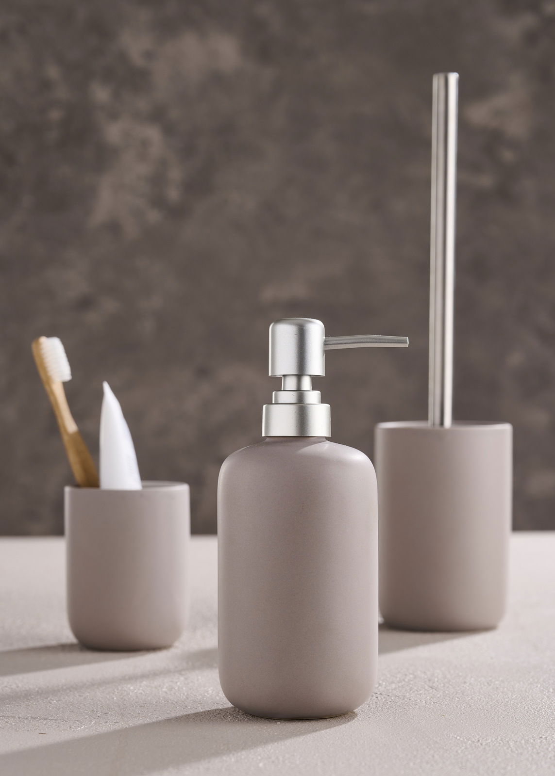 Modernes dreiteiliges Badset in neutralen Tönen, bestehend aus Seifenspender, Zahnbürstenhalter und Toilettenbürstenhalter, aus seitlicher Perspektive fotografiert.