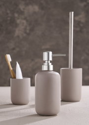 Modernes dreiteiliges Badset in neutralen Tönen, bestehend aus Seifenspender, Zahnbürstenhalter und Toilettenbürstenhalter, aus seitlicher Perspektive fotografiert.