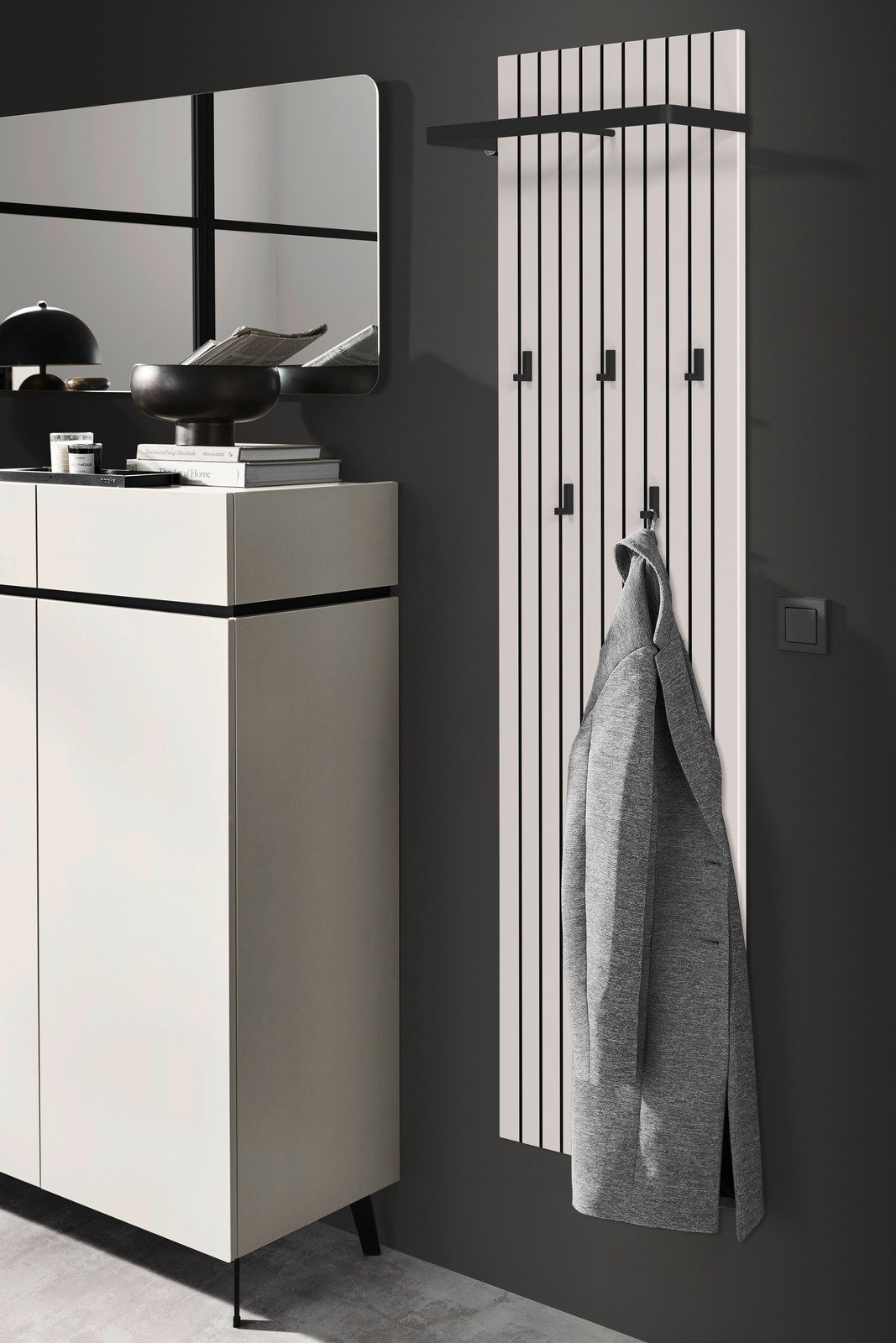 Modernes Garderobenpaneel mit vertikalen Streifen und mehreren Haken, an dem ein grauer Mantel hängt. Perspektive von der Seite.