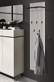 Modernes Garderobenpaneel mit vertikalen Streifen und mehreren Haken, an dem ein grauer Mantel hängt. Perspektive von der Seite.