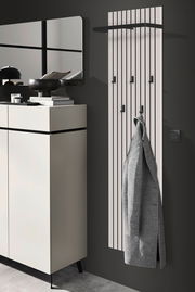Modernes Garderobenpaneel mit vertikalen Streifen und mehreren Haken, an dem ein grauer Mantel hängt. Perspektive von der Seite.