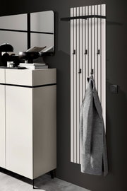 Modernes Garderobenpaneel mit vertikalen Streifen und mehreren Haken, an dem ein grauer Mantel hängt. Perspektive von der Seite.