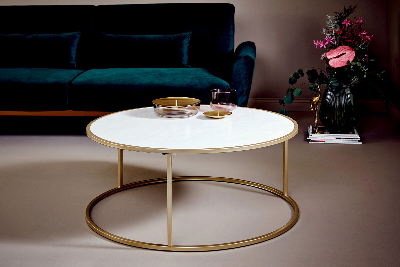 Runder Couchtisch mit weißer Tischplatte und goldfarbenem Gestell, seitliche Perspektive, im Wohnzimmer mit grünem Sofa und Blumenarrangement.