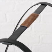 Nahaufnahme eines Kaminholzregals mit schwarzem Metallrahmen und braunem Ledergriff, seitliche Perspektive.