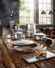 Elegantes 9-teiliges Topf-Set Diamant aus Edelstahl, präsentiert auf einem rustikalen Holztisch in einer modernen Küche mit großen Fenstern im Hintergrund. Perspektive von vorne.