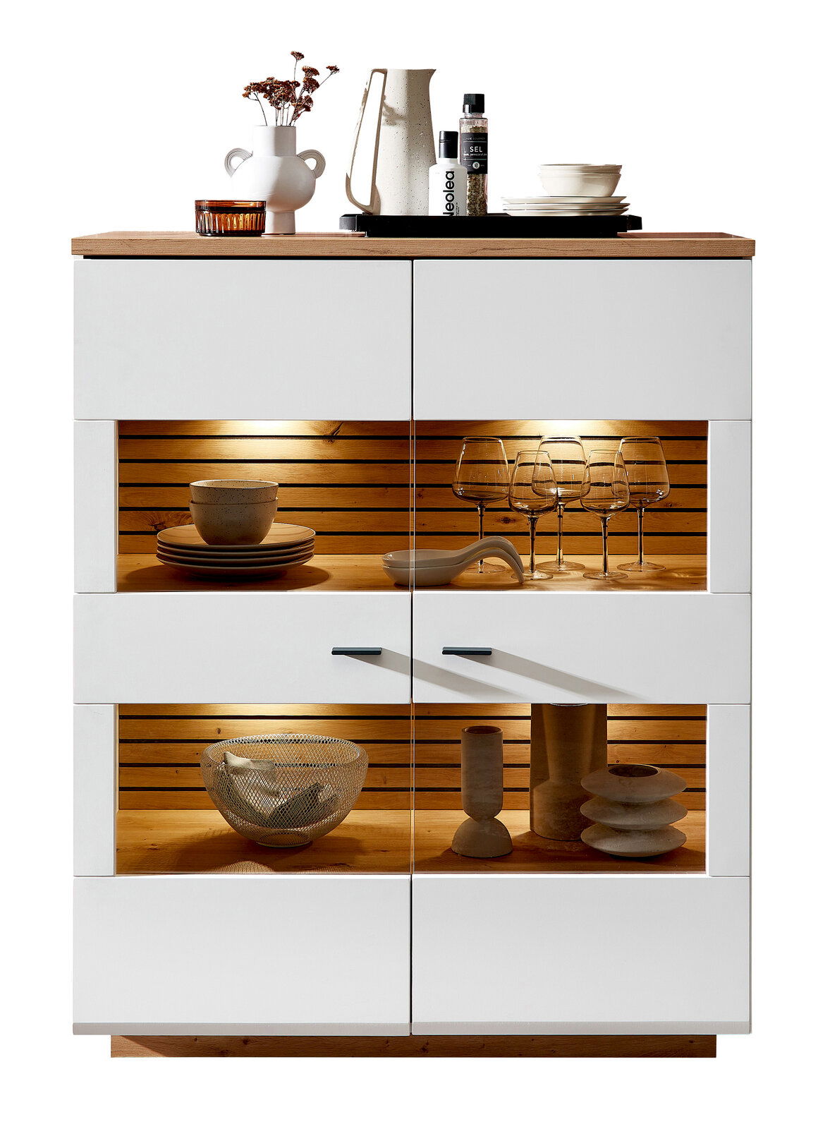 Frontansicht des Highboards Zurbrüggen FRESNO mit weißem Korpus, Holzdetails und integrierter Beleuchtung, dekoriert mit Geschirr und Gläsern.