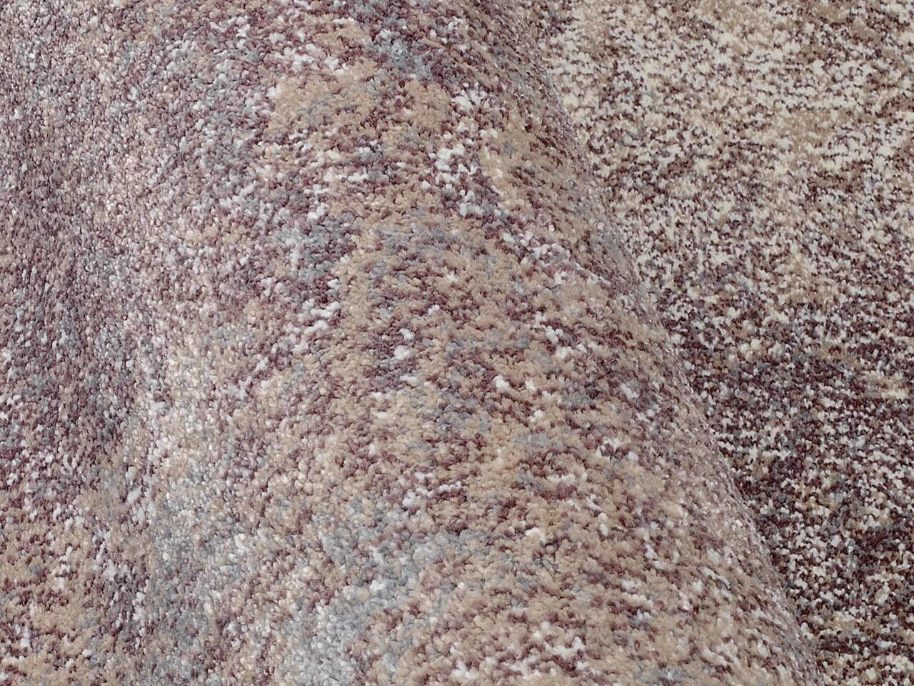 Nahaufnahme eines Designer Teppichs mit melierter Textur in Beige- und Grautönen, seitliche Perspektive