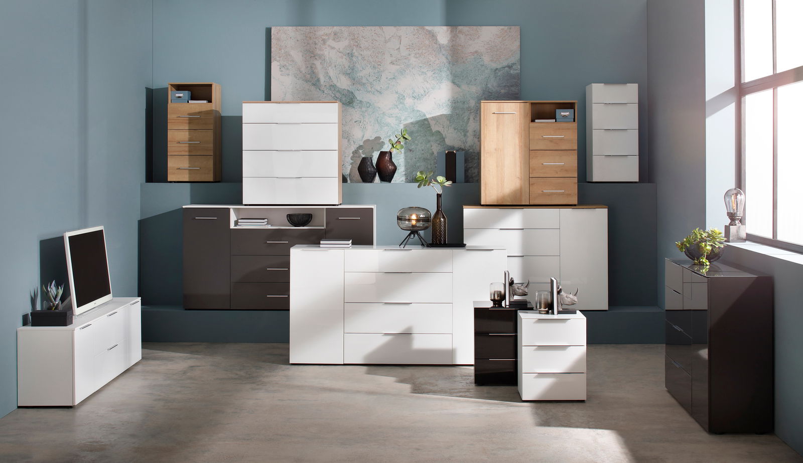 Moderne Kommoden und Sideboards in verschiedenen Größen und Farben, frontal präsentiert in einem stilvollen Raum mit blauer Wand und großem Fenster.