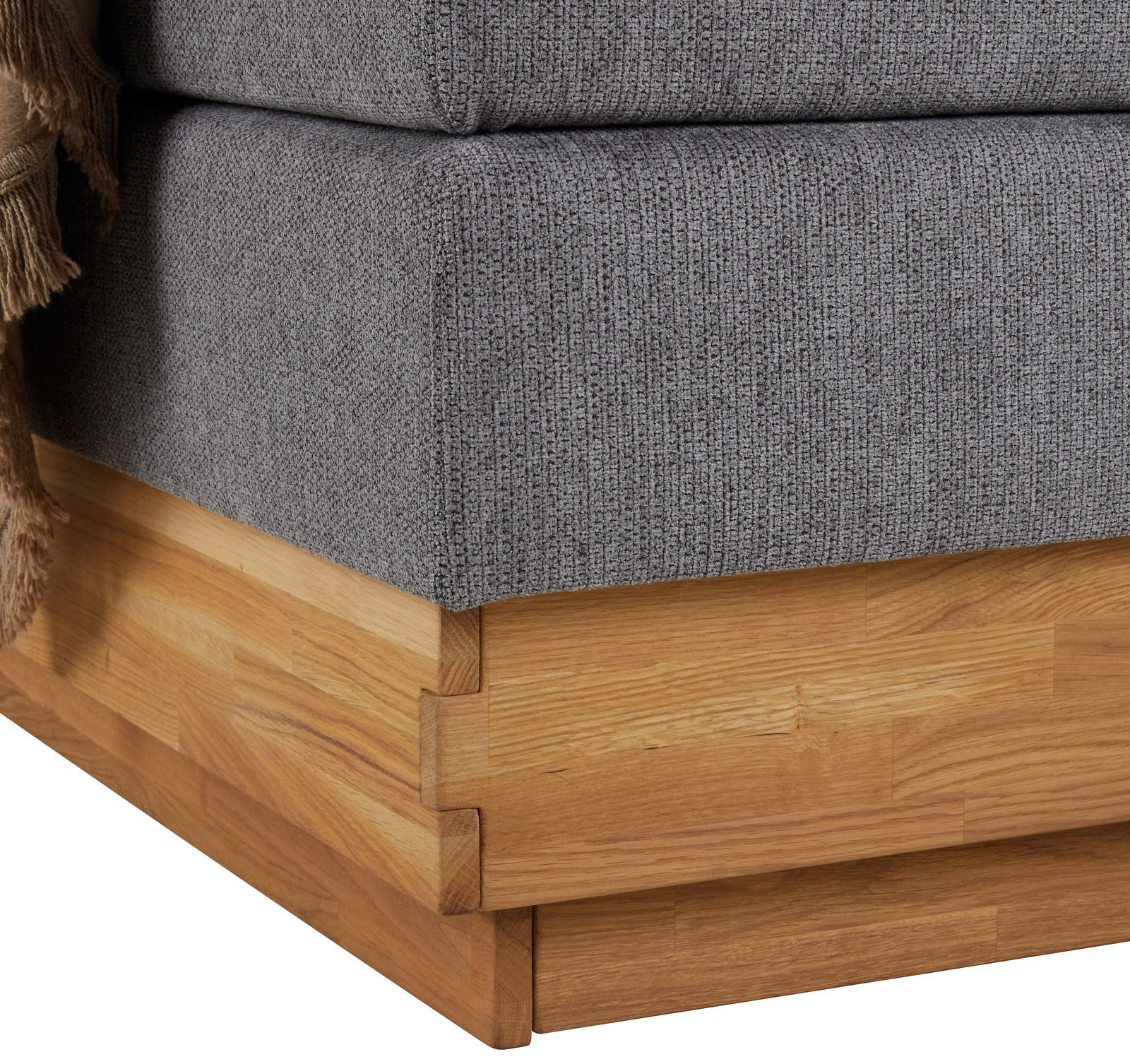 Nahaufnahme der Ecke eines Boxspringbetts mit grauem Stoffbezug und Holzrahmen.