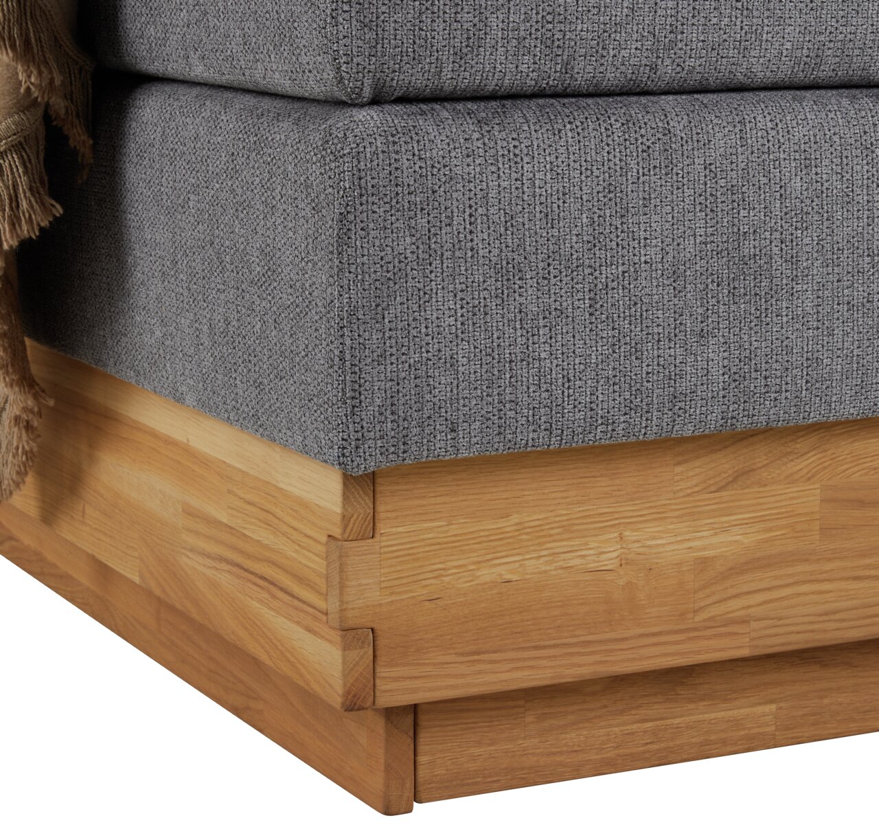 Nahaufnahme der Ecke eines Boxspringbetts mit grauem Stoffbezug und Holzrahmen.