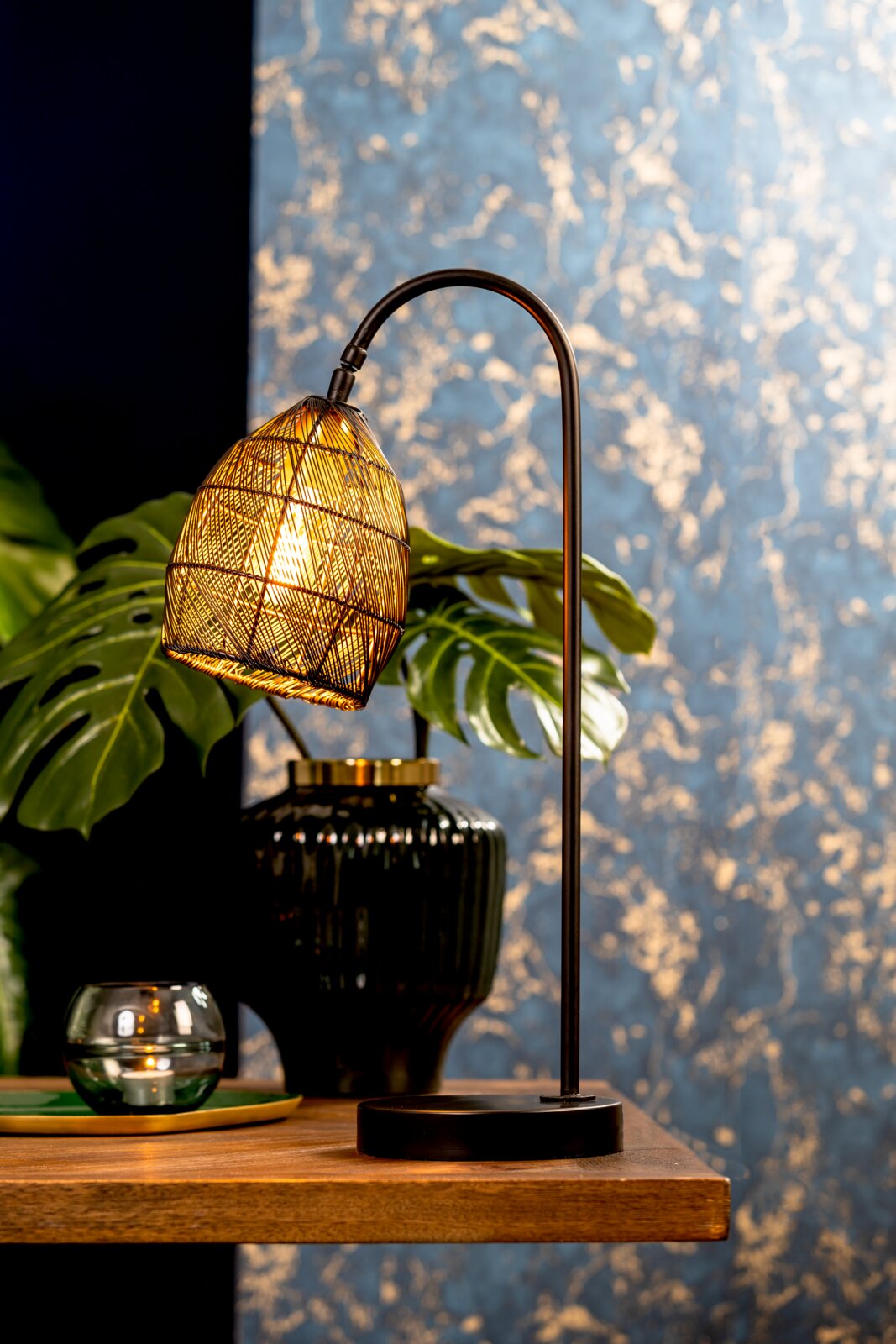 Light&Living Tafellamp MEYA Sfeervolle zwarte tafellamp met gebogen standaard en warm verlichte, gevlochten kap, vanuit schuin vooraanzicht gefotografeerd op een houten tafel.