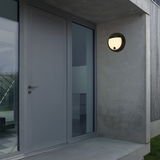 Moderne runde Akku-Außenwandleuchte an einer Betonwand neben einer Haustür, seitliche Perspektive