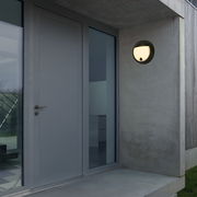 Moderne runde Akku-Außenwandleuchte an einer Betonwand neben einer Haustür, seitliche Perspektive