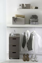 Korb A6 Country aus Porzellan in einem modernen, hellen Raum, auf einem Regal platziert, mit gefalteten Kleidungsstücken und Accessoires. Perspektive von vorne.