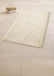 Beige-weißer Badteppich mit Streifenmuster auf Fliesenboden, perspektivisch von oben fotografiert.