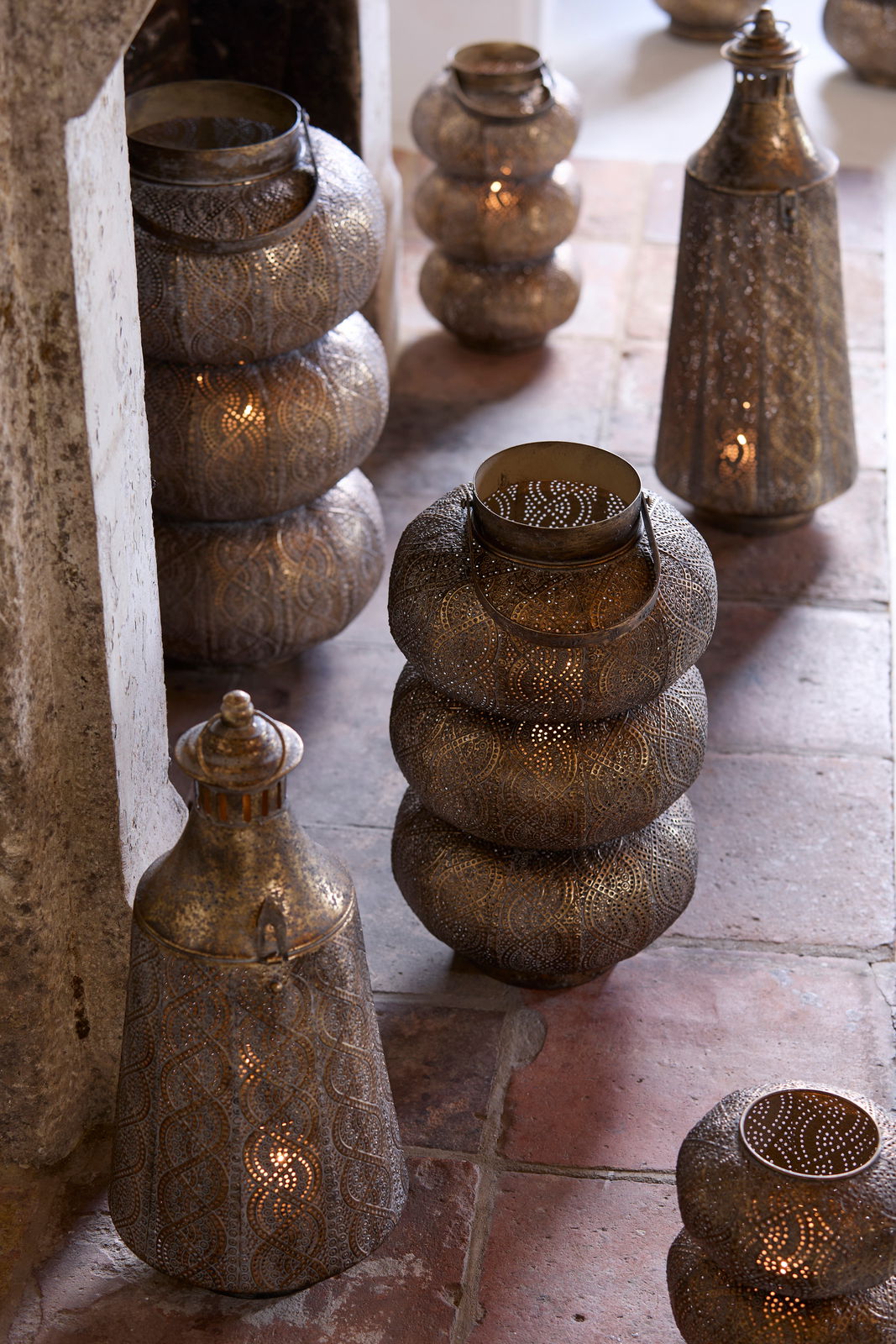 Light&Living Windlicht SANYA 53,5cm Mehrere dekorative Windlichter aus Metall mit filigranen Mustern, die auf einem Boden aus Steinfliesen stehen. Die Perspektive zeigt die Windlichter von schräg oben.