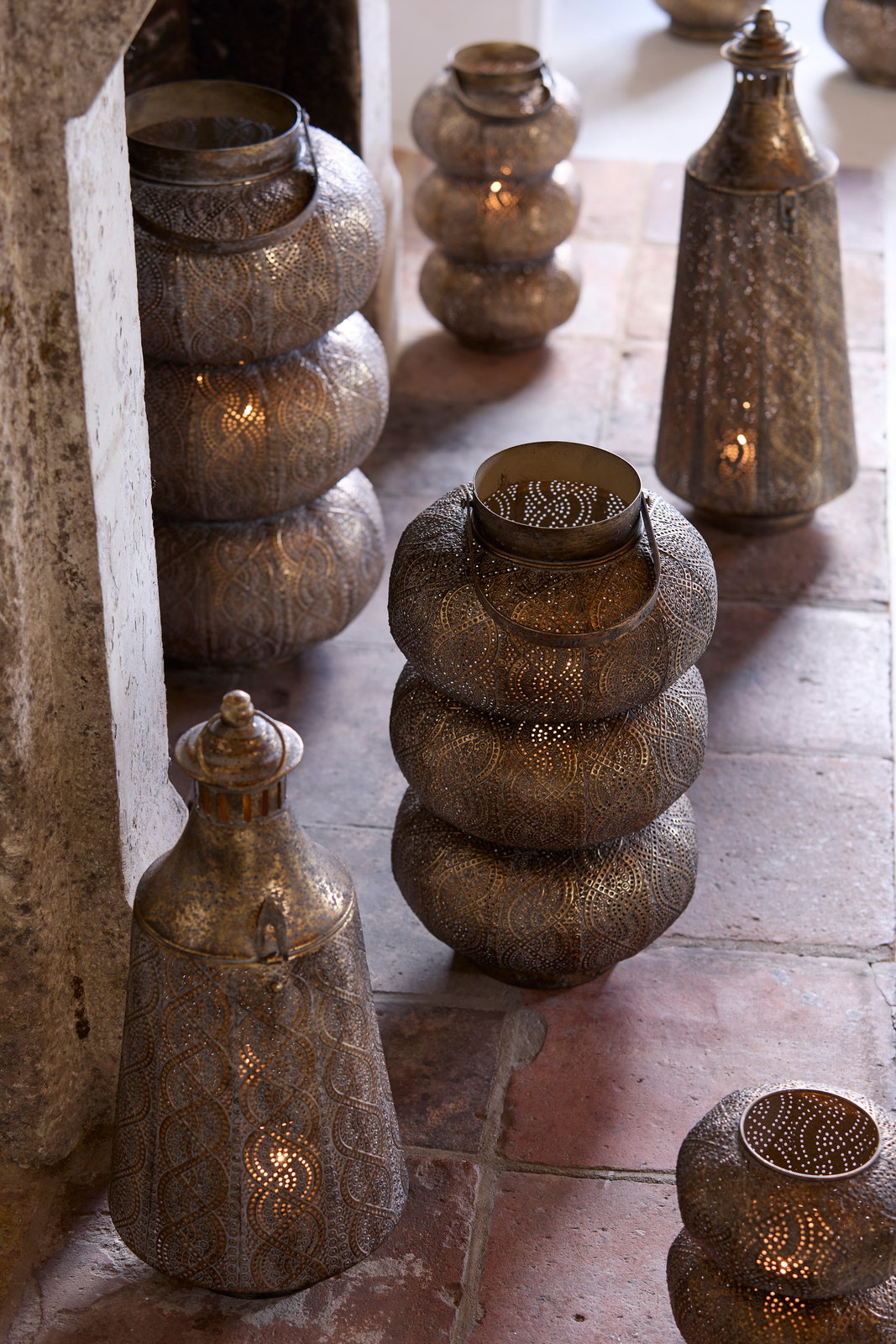 Light&Living Windlicht SANYA 53,5cm Mehrere dekorative Windlichter aus Metall mit filigranen Mustern, die auf einem Boden aus Steinfliesen stehen. Die Perspektive zeigt die Windlichter von schräg oben.