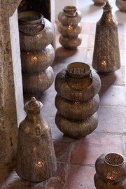 Mehrere dekorative Windlichter aus Metall mit filigranen Mustern, die auf einem Boden aus Steinfliesen stehen. Die Perspektive zeigt die Windlichter von schräg oben.