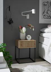 Moderne Nachtkommode aus Holz mit schwarzem Metallgestell, dekoriert mit einer Pflanze und einer Uhr, seitliche Perspektive.