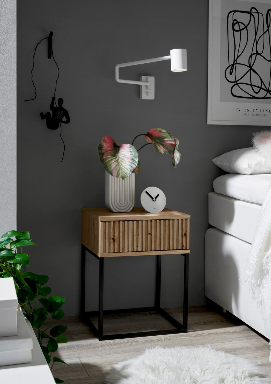 Moderne Nachtkommode aus Holz mit schwarzem Metallgestell, dekoriert mit einer Pflanze und einer Uhr, seitliche Perspektive.