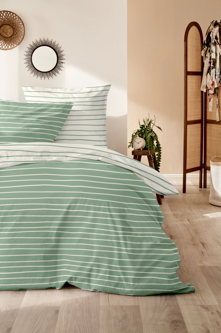 Grün-weiß gestreifte Bettwäsche in einem gemütlichen Schlafzimmer, seitliche Perspektive
