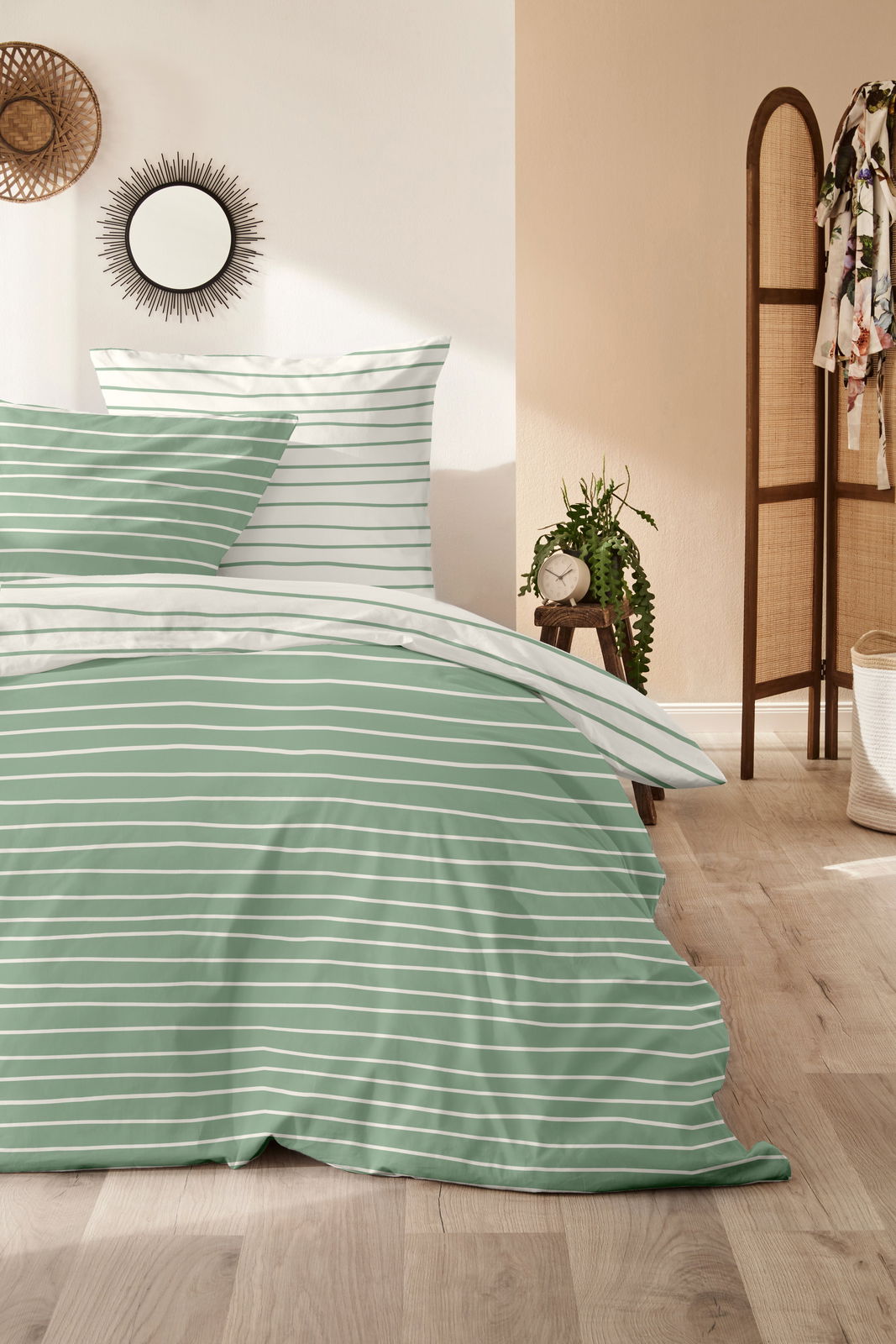 Grün-weiß gestreifte Bettwäsche in einem gemütlichen Schlafzimmer, seitliche Perspektive