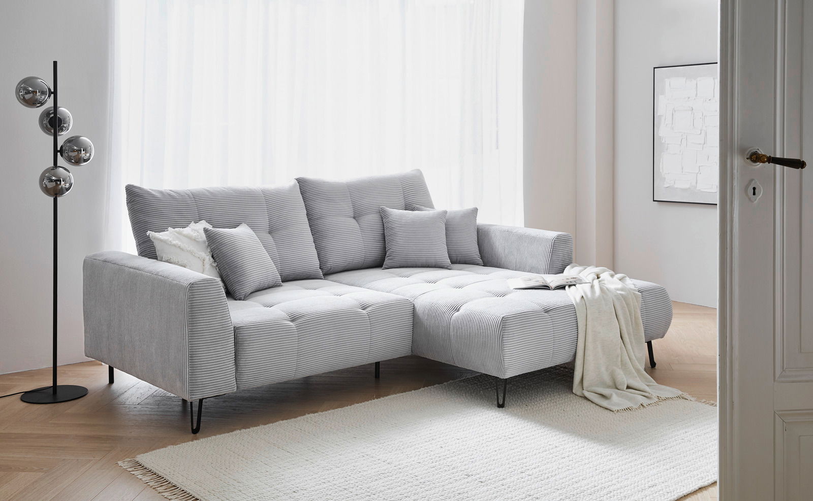 Graues Ecksofa SWING mit Ottomane, dekoriert mit Kissen und Decke, in einem hellen Wohnzimmer, seitliche Perspektive.