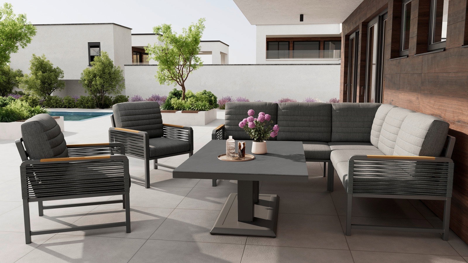 Moderne Loungegarnitur auf einer Terrasse mit Blick auf einen Garten und Pool, bestehend aus einem Ecksofa, zwei Sesseln und einem Tisch.