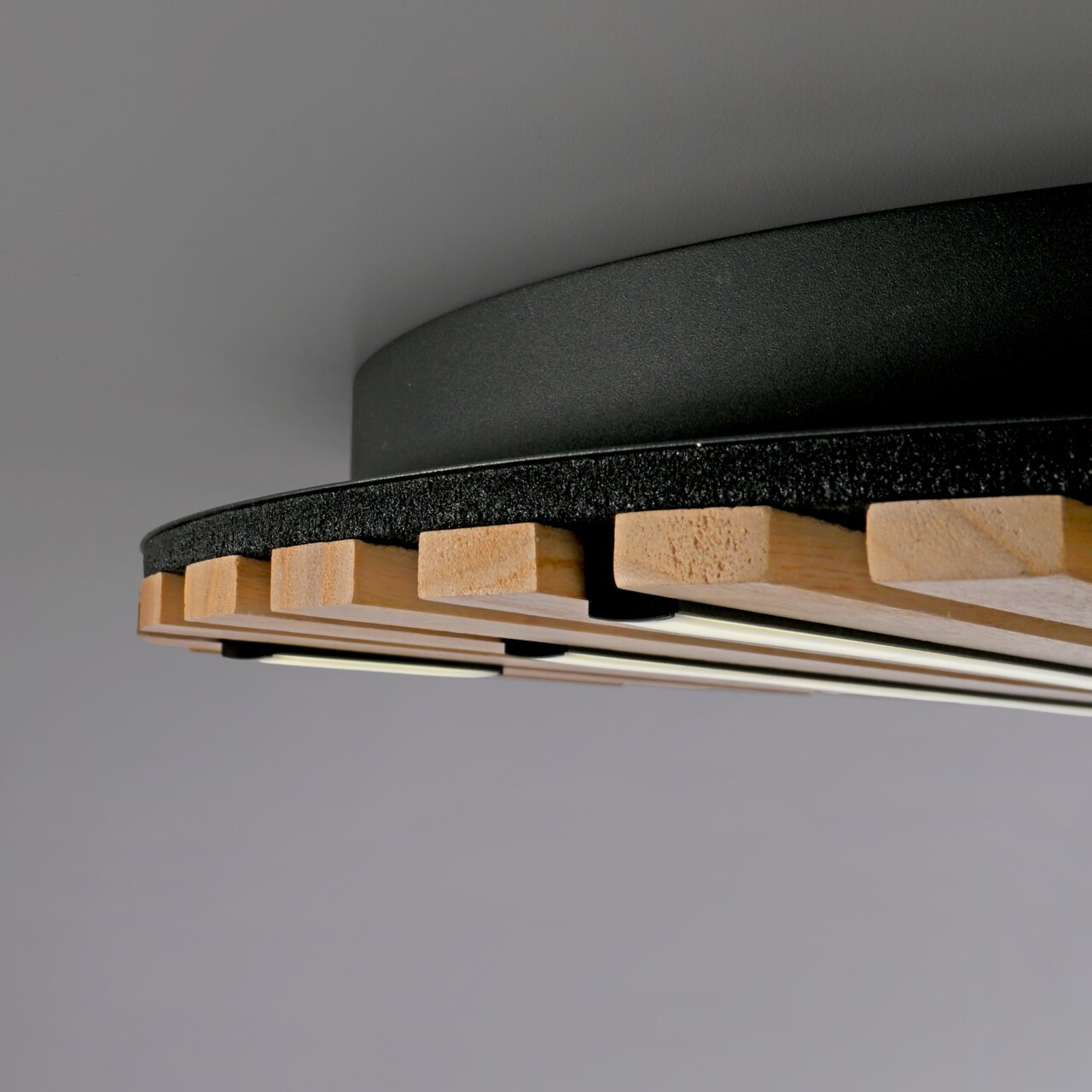 Nahaufnahme der Paul Neuhaus Wand- und Deckenleuchte Q-AKUSTIK mit Holz- und Metallelementen, von unten betrachtet.