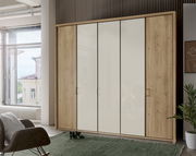 Moderner 5-türiger Drehtürenschrank in Holzoptik mit weißen Fronten, fotografiert aus einer frontalen Perspektive in einem hellen Raum.