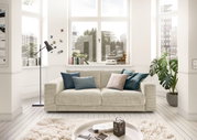 Zweisitzer-Sofa in einem hellen Wohnzimmer mit großen Fenstern, dekoriert mit bunten Kissen, aus der Frontperspektive.