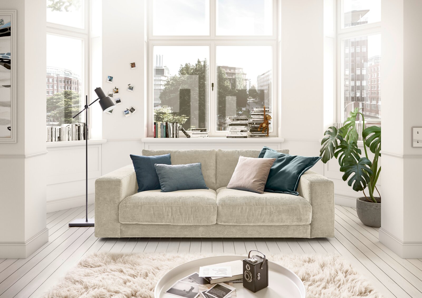 Zweisitzer-Sofa in einem hellen Wohnzimmer mit großen Fenstern, dekoriert mit bunten Kissen, aus der Frontperspektive.