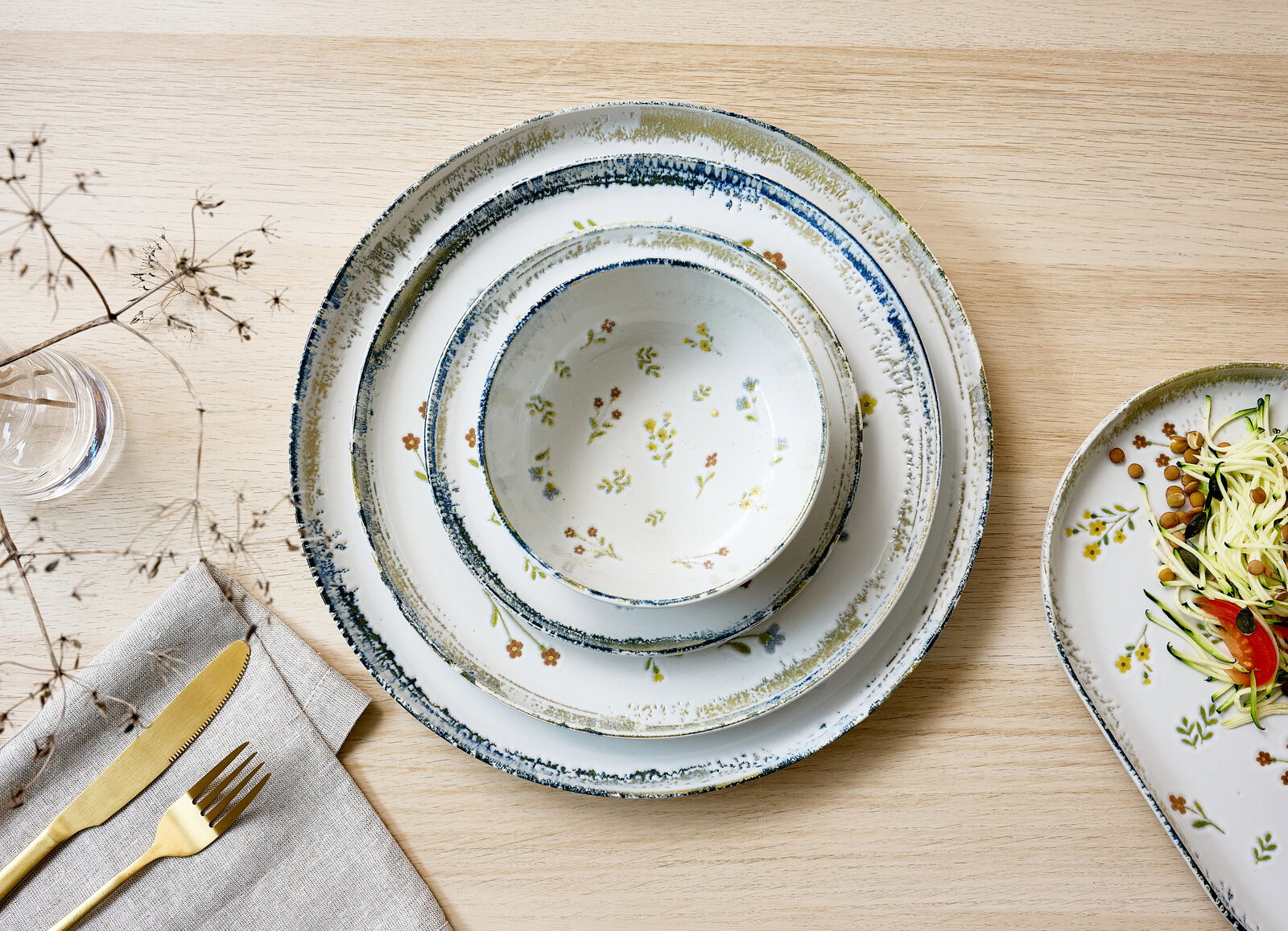 Dreiteiliges Keramik-Geschirrset mit Schale und zwei Tellern in Weiß mit blauem Rand und zartem Blumenmuster, Draufsicht auf hellem Holztisch.