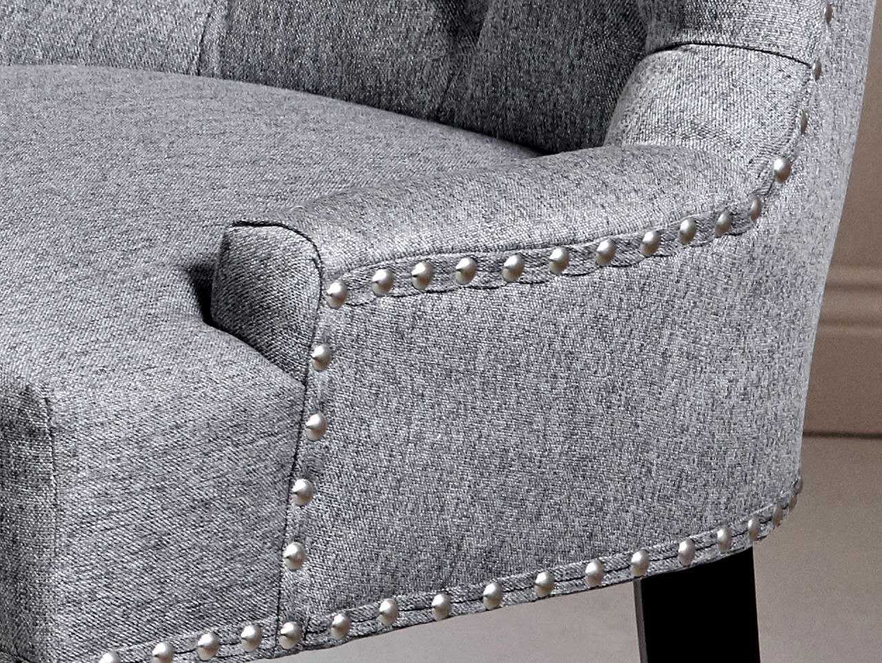 Detailansicht eines grauen Stuhls mit Nietenverzierung und dunklen Holzbeinen.