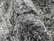 Nahaufnahme eines Designer-Teppichs mit abstraktem Muster in Grautönen, aus seitlicher Perspektive aufgenommen.