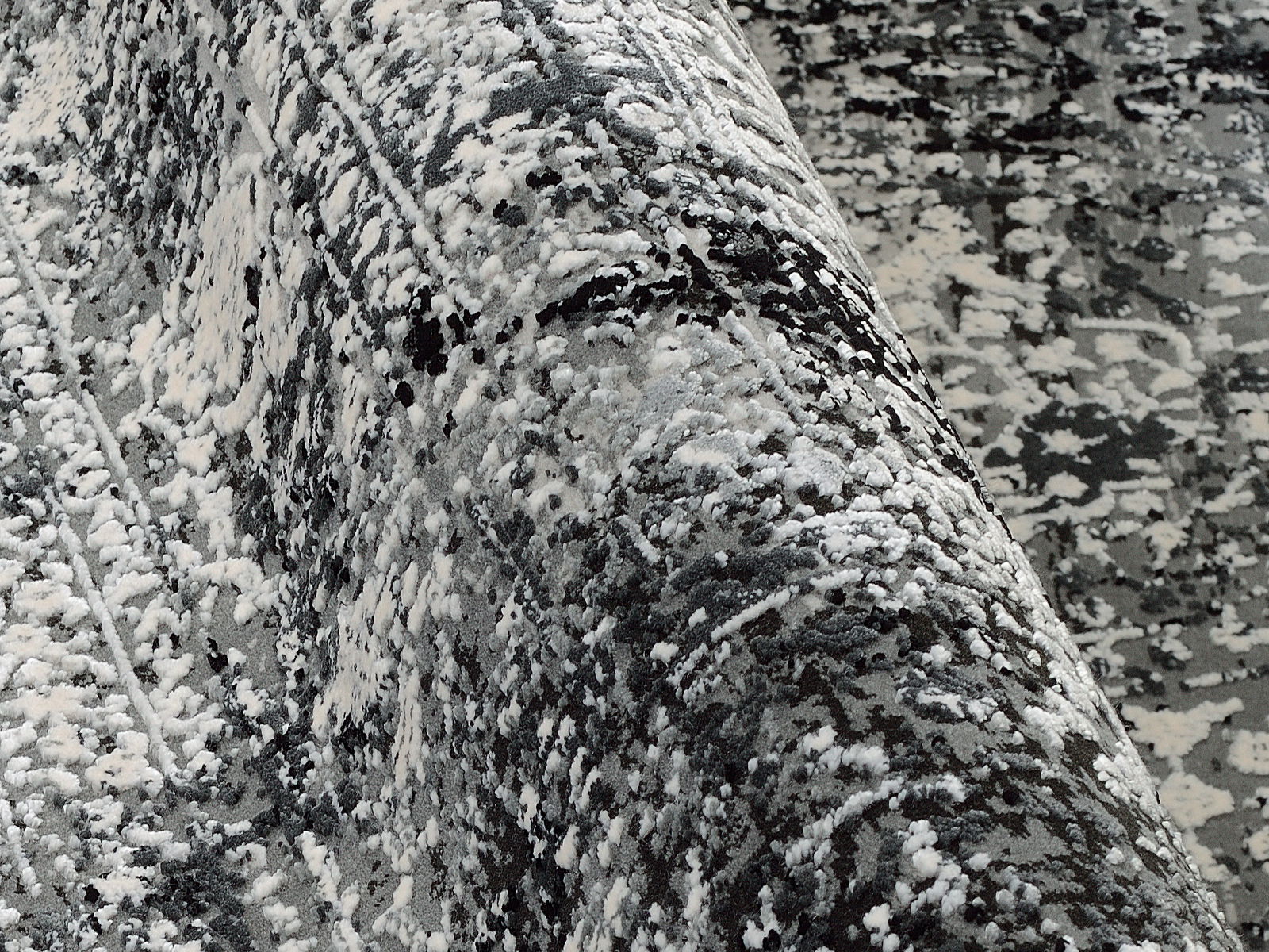 Nahaufnahme eines Designer-Teppichs mit abstraktem Muster in Grautönen, aus seitlicher Perspektive aufgenommen.