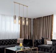 Moderne Hängeleuchte mit vier zylinderförmigen, goldenen Lampenschirmen, die von der Decke in einem eleganten Wohnzimmer mit dunklen Sofas und einem Glastisch hängt. Perspektive von schräg unten.