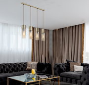 Moderne Hängeleuchte mit vier zylinderförmigen, goldenen Lampenschirmen, die von der Decke in einem eleganten Wohnzimmer mit dunklen Sofas und einem Glastisch hängt. Perspektive von schräg unten.