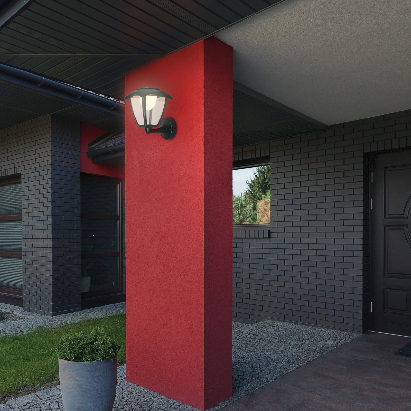 Außenansicht eines modernen Hauses mit einer Akku-Außenwandleuchte an einer roten Wand, seitliche Perspektive.